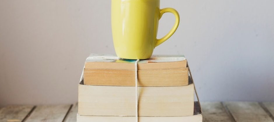 Banner do diário da Livraria Ipê: pilhas de livros novos e usados, uma xícara de café e luz suave de tarde sobre a mesa